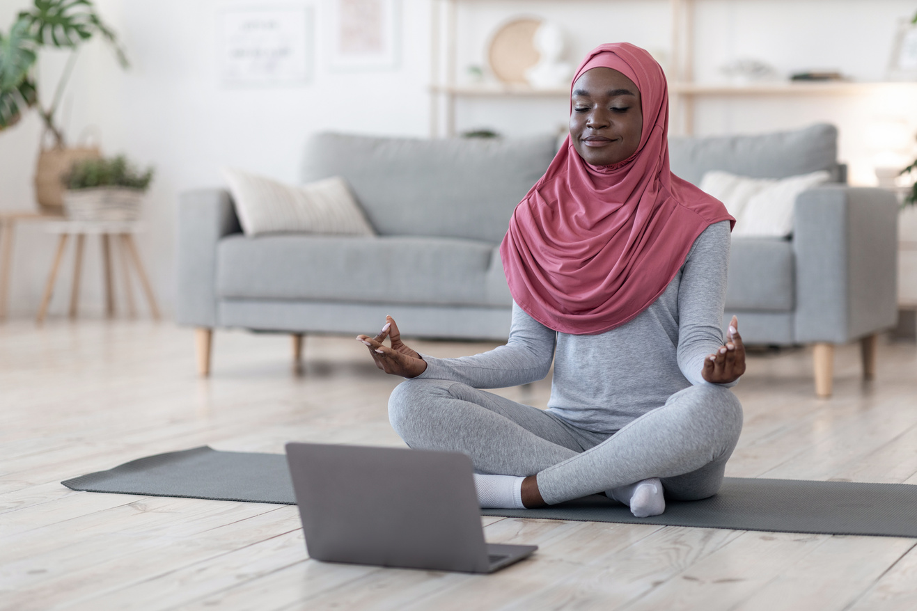 Yoga online. Black muslim woman meditating in front of laptop at home